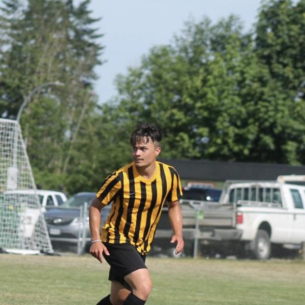A young man in yellow-and-black striped shirt playing soccer. 