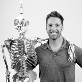 A smiling man holding a human skeleton. 