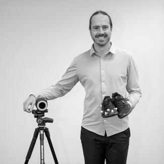 A smiling man holding his shoes. 